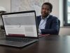 Close-up of a laptop screen showing a professionally designed website still loading, with a Port Harcourt business owner watching in the background.