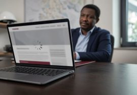 Close-up of a laptop screen showing a professionally designed website still loading, with a Port Harcourt business owner watching in the background.